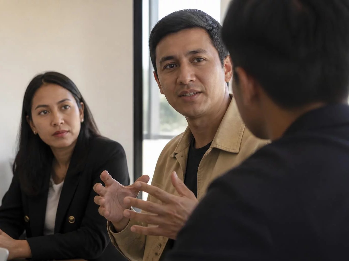 Tres profesionales en una sala de reuniones clara, uno de ellos explicando