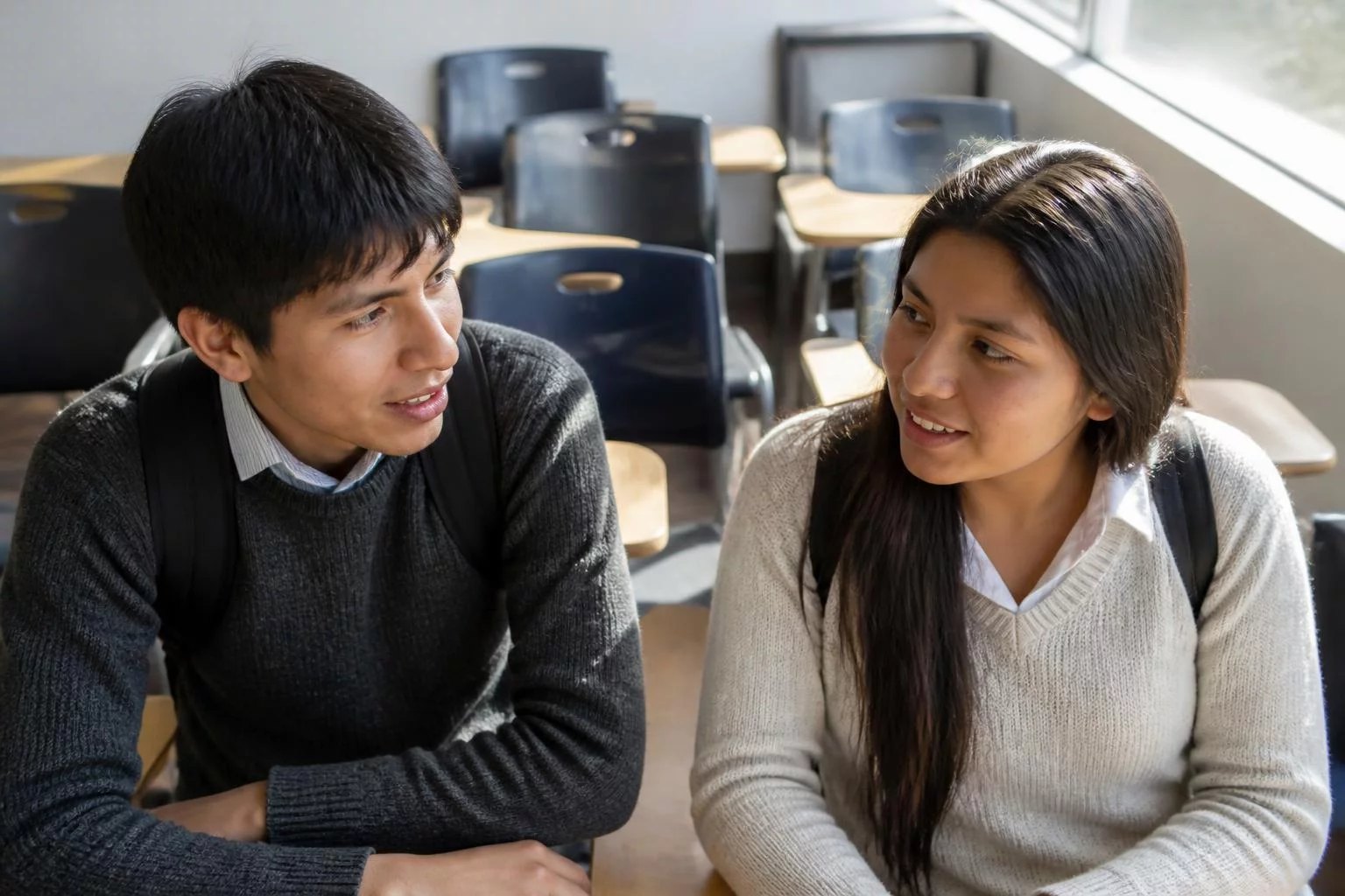 Dos estudiantes con mochila conversando en un pasillo universitario